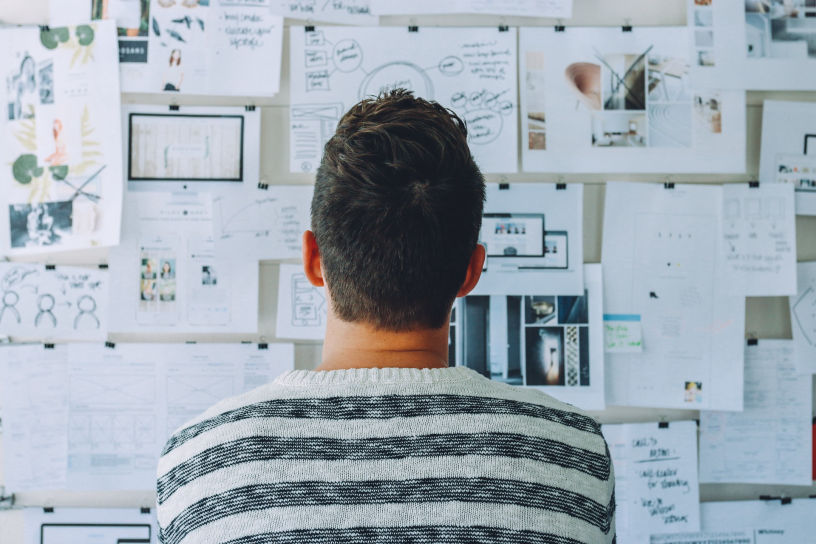 man staring at a pin board full of papers and drawings